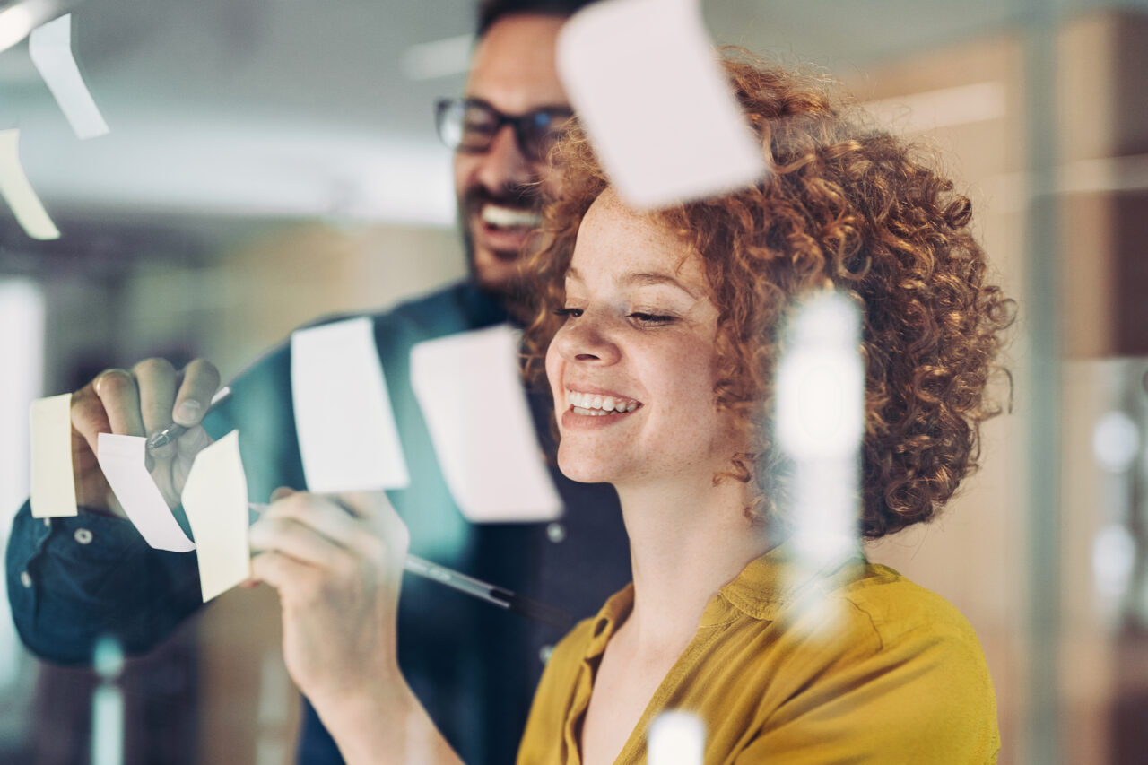 Ein Mann und eine Frau schreiben auf Post-It's an einer Wand