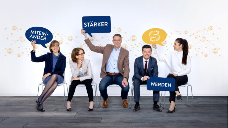 ÖGV Team - 2 Männer und 3 Frauen sitzen auf Bürostühlen, sie halten zum Teil Sprechblasen mit Text in den Händen, die zusammengesetzt die Aussage "Miteinander stärker werden" ergeben.